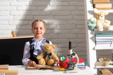 Okula dönelim. Mutlu şirin çocuk bir masada oturmuş oyuncak ayıyı tutuyor. Çocuk sınıfta öğreniyor.