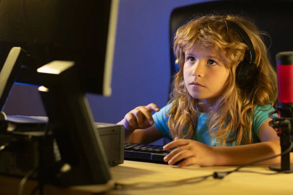 Child plays a video game on the pc computer screen. Portrait of cute child while typing on keyboard. Gamer play computer games. Neon lighting