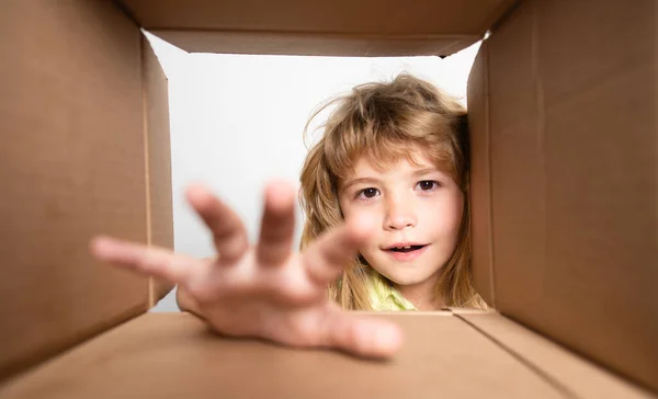 Kid unpacking and opening carton box, and looking inside with surprise face. Open box and delivery parcel for children