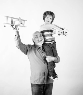 Gelecek nesil aile rüyası. Mavi arka planda oyuncak uçağı olan mutlu büyükbaba ve torun izole edildi. Mutlu büyükbaba, torununu sırtında taşıyor.