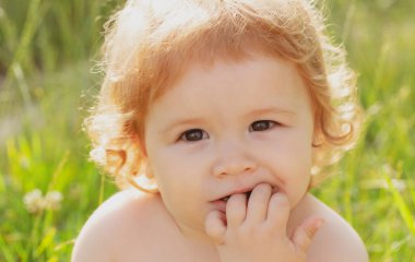 Yazın çimenlikteki bebek. Bebek yüzlü, yakın çekim. Küçük komik çocuk portresi. Sarışın çocuk, duygusal yüz.