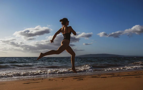 Woman running along ocean surf by water pool to keep fit and health. Woman fitness, jogging workout and sport activity on summer holiday