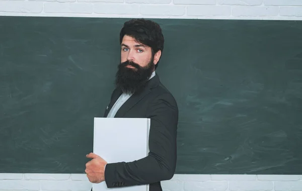 Teachers day - knowledge and educational school concept. Bearded professor at school lesson at desks in classroom. Preparing for exam in college. Young teacher