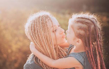 Gülümseyen annenin sevimli küçük kızına sarılma portresi. Küçük kızıyla birlikte gün batımında gülümseyen mutlu anne portresi.