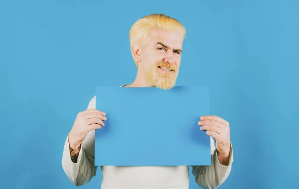 Portrait of man showing blue blank signboard with copy space area for slogan or text. Young man shows a sheet of paper in the camera on a color background. Copy space