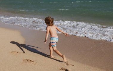 Çocuk yaz tatilinde plajda oynuyor. Doğadaki çocuklar, deniz suyunda akan kumlar ve mavilikler.