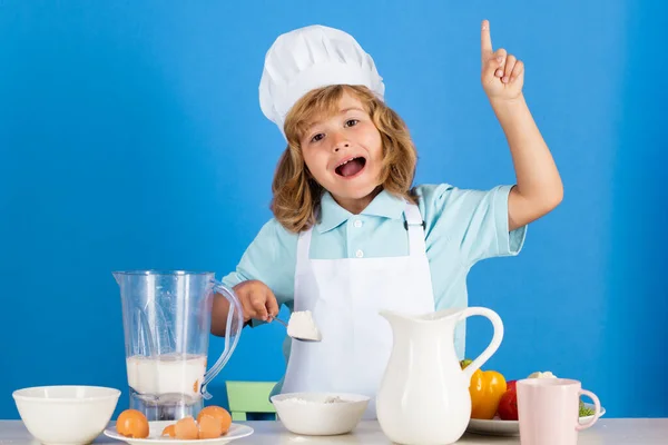 Kid boy in chef hat and apron cooking preparing food with flour. Little cook with vegetables at kitchen. Natural kids food