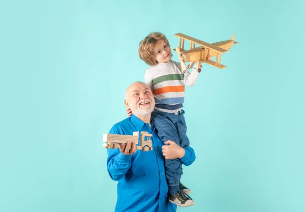 Young grandson and old grandfather piggyback with toy plane and wooden truck. Men generation granddad and grandchild