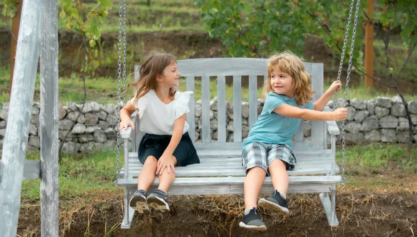兄と妹が外で揺れている 庭で働いている男の子と女の子 夏の公園で2人の幸せな子供 子供の夏休みの休暇の概念 子供の友情 — ストック写真