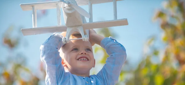 木製のおもちゃの飛行機で遊んでいる子供の男の子 パイロットになる夢 子供たちの夢 木製の飛行機で子供パイロット航空機 ブロンドの子供笑顔の感情の顔 — ストック写真