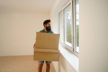 Adam eşyalarını kutularda taşıyor. Yeni bir daireye taşınıyorum. Karton kutuları olan mutlu genç bir adam.