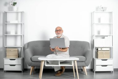 Üst düzey ofis çalışanının dizüstü bilgisayarlı portresi. Gri sakallı yaşlı adamın evde ya da ofiste bir dizüstü bilgisayarda işi var. Bilgisayar kullanan olgun yaşlı bir adam. Yaşlı genel müdür.