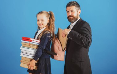 Öğretmen okul çocuğu için okul malzemeleriyle sırt çantası hazırlıyor. Elinde kitap yığını olan küçük bir kız. Çalışması zor.