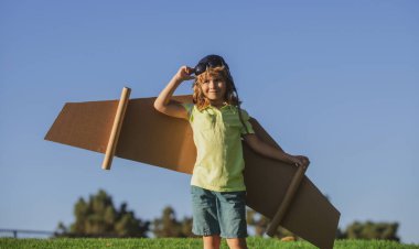 Pilot olacak çocuk. Kağıt kanatlı çocuk uçuyor. Yaz tatili ve seyahat konsepti. Oyuncak karton uçak kanatlarıyla gökyüzünde uçan komik çocuk. Başlangıç özgürlüğü ve çocukların tasasız konsepti