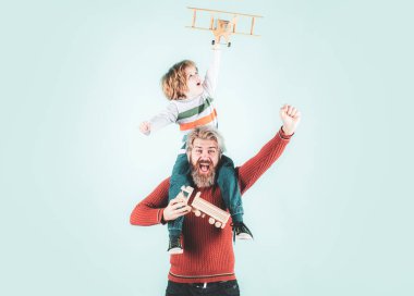 Baba ve Oğul oyuncaklarla oynuyor, sarılıyor, kameraya bakıyor ve gülümsüyor. Baba oğlunu sırtında taşır, mavi üzerine izole eder.