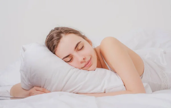 年轻女人躺在床上 抱着柔软的白色枕头睡得很好 女孩休息 女人在睡觉美丽的年轻女子躺在床上 两眼紧闭 毛毯盖住 — 图库照片