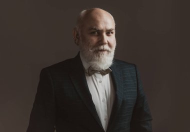 Takım elbiseli ve kravatlı kendinden emin yaşlı sakallı adam gri izole arka planda duruyor. Moda kıyafetli yetişkin adam pozu