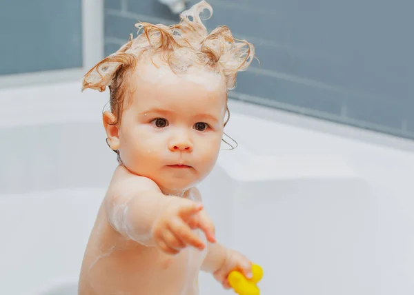 浴槽でお風呂に入ることで水遊びを楽しんでいる面白いブロンドの少年 入浴中の赤ん坊 頭の上に石鹸泡を持つ幸せな子供 — ストック写真