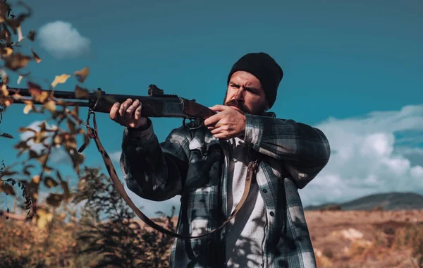 Bearded hunter man holding gun and walking in forest. Hunter with shotgun gun on hunt. Big game