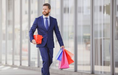 Alışveriş torbaları tutan ve alışveriş mağazasında yürüyen bir iş adamı. Alışveriş ve ödeme. Alışverişkolik alışveriş kavramı
