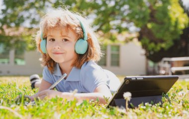 Çocuk mesafesi öğrenme konsepti. Uzaktan eğitim, okul parkında online ders alan bir çocuk. Kalemle kitap yazan bir öğrenci, açık havada çalışmaz. Kendi kendine öğrenim öğrenme. Erken gelişim