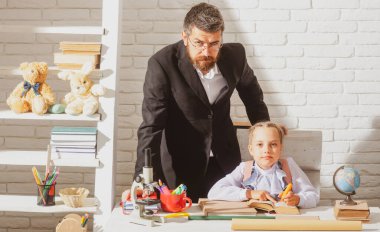 Öğretmen, öğrenci kıza okuldaki görevinde yardım ediyor.