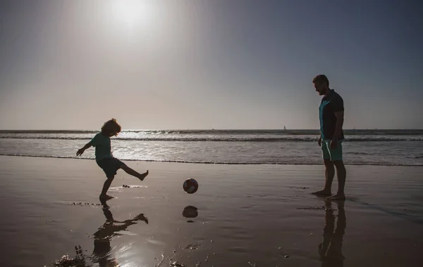 父と息子はビーチでサッカーやサッカーをします 夏の日に遊んでいる子供の男の子とパパ — ストック写真