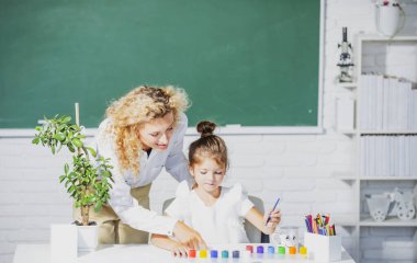 Okula dönelim. Anne ve kızı birlikte resim yapıyorlar. Öğretmen kıza yardım ediyor.