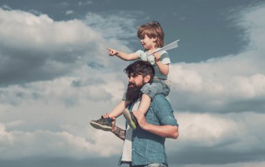 Baba ve oğul. Çocuk babasının omuzlarında oturuyor. Nesil. Mutlu çocuk kağıt uçak ile oynuyor