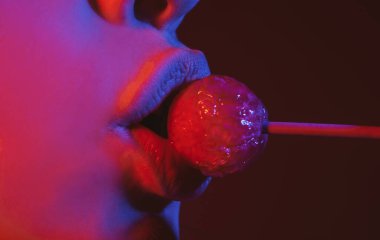 Dudakları emiyor. Ağzında kırmızı lolipop şekeri tutan pembe rujlu yakın plan kadın dudakları. Yüzünde lolipop var.