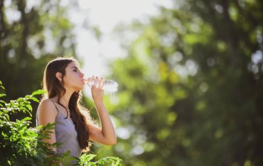 Şişeden su içen sağlıklı bir kadın. Susuz kalma konsepti. Susuz kalmış. Doğayla birlik, açık hava