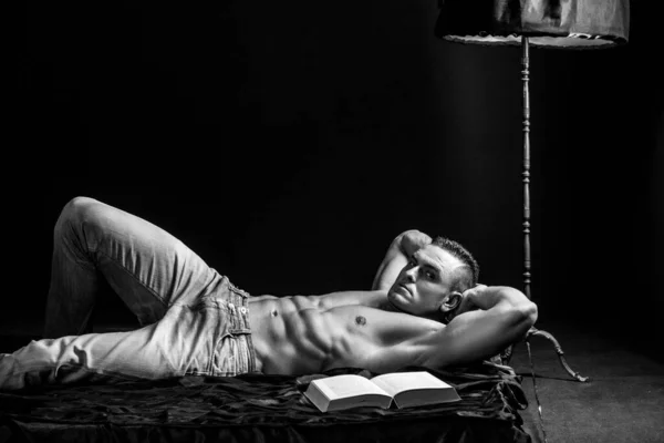 寝室で読書 本と裸の胴とブルーデニムでハンサムな男 ベッドに寝そべって ラグジュアリーライフスタイル — ストック写真