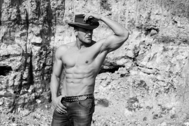 Kaslı vücutlu bir adam dışarıda üstsüz poz veriyor. Seksi iri kıyım. Kaslı, çıplak gövde. Altı paket kaslı göğüs. Kotlu ve kovboy şapkalı yakışıklı, kaslı, üstsüz adam.