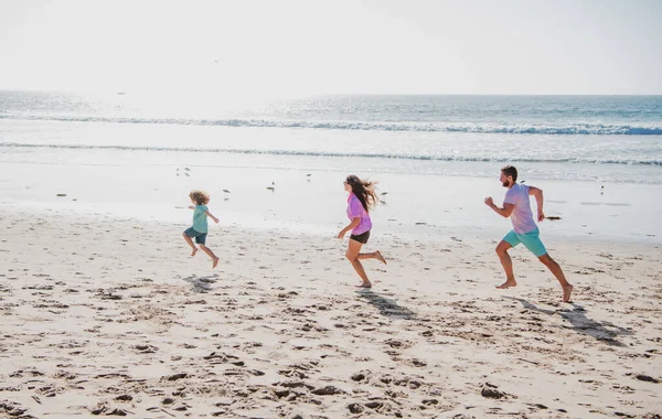 幸せな若い家族が走り 夏のビーチでジャンプします フレンドリーな家族と夏休みの概念 親が走って飛び跳ねる子 — ストック写真