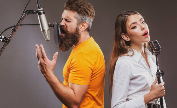 Singer duet couple is performing a song with a microphone while recording in a music studio