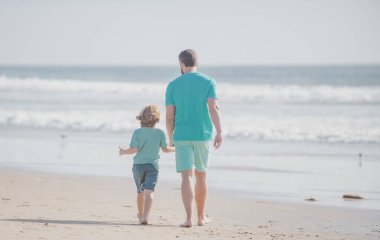 Baba ve oğul yaz plajında yürüyor. Arkadaş canlısı aile kavramı ve yaz tatili