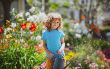 Yaz günü bahçede bitkileri sulayan tatlı bir çocuk. Bahçede bahçe aletleri ve su bidonu olan bir çocuk.