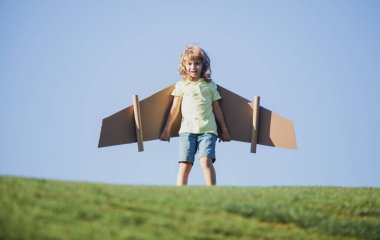 Pilot olacak çocuk. Kağıt kanatlı çocuk uçuyor. Yaz tatili ve seyahat konsepti. Oyuncak karton uçak kanatlarıyla gökyüzünde uçan komik çocuk. Çocuklar yazın doğada seyahat etmeyi hayal ederler.