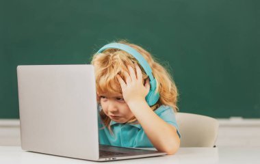 Kızgın üzgün çocuk kulaklık takıyor, sınıfta dizüstü bilgisayarla çalışıyor, müzik dersi dinliyor.