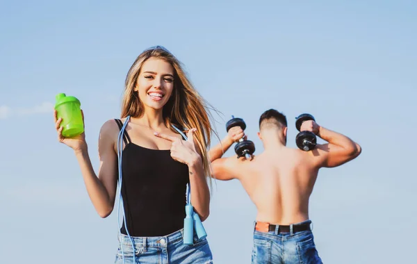 Slim woman trainer of fitness with protein shaker. Smiling young female and personal couple coach. Man and girl with protein shake bottle and skipping rope