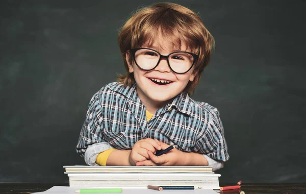 Back to school and happy time. Funny little boy in glasses on blackboard background. Kid with a book