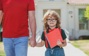 İlkokulun ebeveyni ve inek öğrencisi el ele gidiyor. Baba sırt çantalı oğlunun elini tutuyor, okula geri dönüyor.