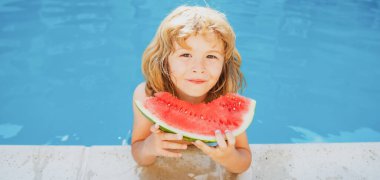 Yüzme havuzunda karpuz yiyen tatlı bir çocuk. Tropikal meyve yemenin tadını çıkar. Yaz çocukları konsepti. Mutlu çocukluk