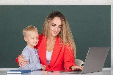 Anne ve oğlu birlikte bilgisayar laptopu kullanıyorlar. Okul çocuğu çevrimiçi eğitim öğreniyor. Öğretmen okul çocuğuna dersi açıklıyor. İlkokul öğrencileri öğreniyor. Anne ve oğul öğreniyor.