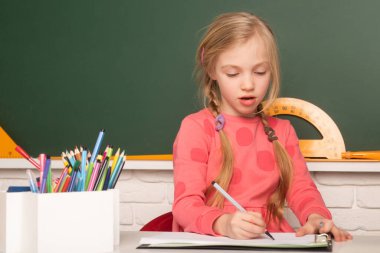 Okulda ödev yapan bir kız. Tahta altyapısı üzerine. İlkokuldan bir çocuk ilkokulda masada oturuyor, not defterine yazıyor ya da çiziyor.