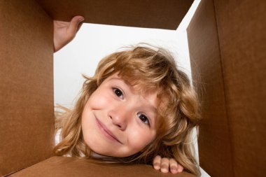 Şaşkın çocuk bavulunu açıyor, kutusunu açıyor ve içine bakıyor. Paket, teslimat, sürpriz, çocuk için hediye. Çocuk duyguları ve çocuk yüz ifadeleri. Yakın çekim çocuk yüzü.