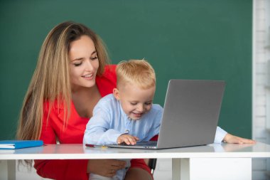 Öğretmen öğrencilerin bilgisayar kullanarak ders almalarına yardımcı oluyor. Anne ve oğul öğreniyor.