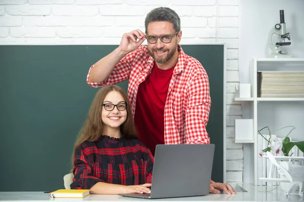 Teacher tutor helping school child in class at school using laptop