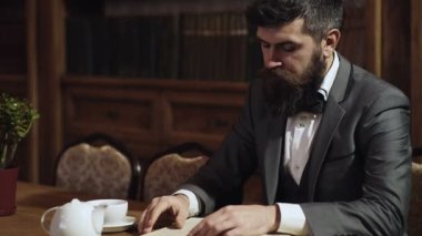 Klasik takım elbiseli konsantre iş adamı kitap okuyor. Eski moda iş adamları. Yakışıklı, iyi giyimli bir adam klasik iç mimarisi olan bir odada kitaplığın yanında duruyor. Eski moda.