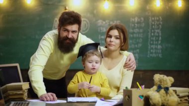 Genç bir aile ders çalışıyor. Ebeveynler çocuklara öğretiyor. Erken gelişim kavramında aile. Baba, anne ve çocuk evde birlikte resim yapıyorlar.